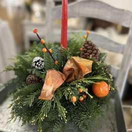 Evergreen centerpiece with red taper candle, pinecones, ribbon, berries, and an orange accent.