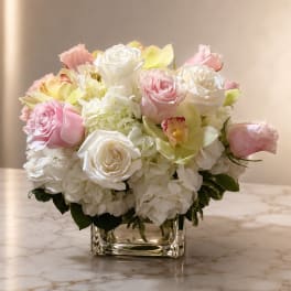 Pink and white roses with orchids in a clear square vase