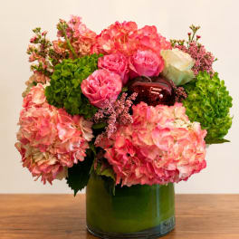 Pink hydrangeas and roses arranged in a green glass vase