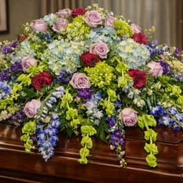 Large floral casket spray with roses, hydrangeas, and hanging blooms