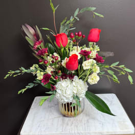 Red roses and white hydrangea in a glass vase with mixed greenery
