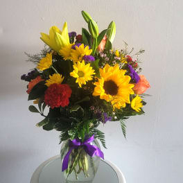 Mixed bouquet of yellow sunflowers, lilies, and roses in a glass vase