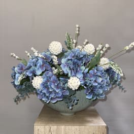Blue hydrangea arrangement in a pale ceramic bowl with white accent flowers