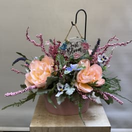 Peach floral arrangement in a pink container with a hanging "Just Bloom" sign