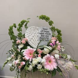 Pink and white floral sympathy arrangement with a heart memorial stone and angel wings