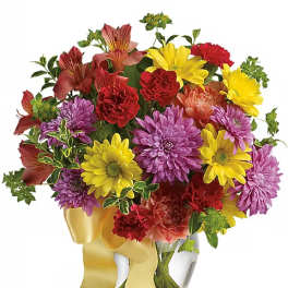 Mixed bouquet of yellow, purple, and red flowers in a glass vase with a yellow ribbon