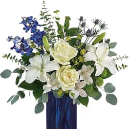 White roses and lilies in a blue glass vase with blue flowers