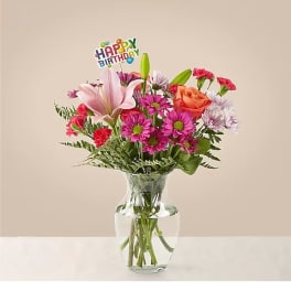 Mixed bouquet in a clear glass vase with a birthday pick