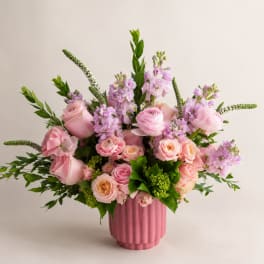 Pink roses and lavender flowers arranged in a pink vase