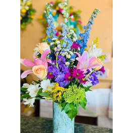 Tall mixed bouquet in a blue ceramic vase with pink lilies and purple flowers