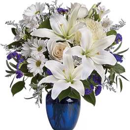 White lilies and daisies arranged in a blue glass vase