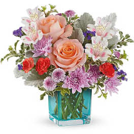 Bouquet of peach roses, white alstroemeria, and purple flowers in a blue glass vase