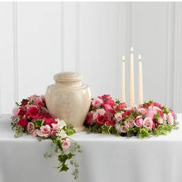 Pink rose arrangements around a beige urn with three candles