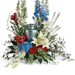 Floral arrangement with red roses, white lilies, blue flowers, and a metal urn