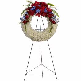 Standing floral wreath with red roses, blue flowers, and white blooms on an easel