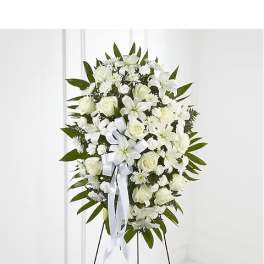 White funeral spray with lilies, roses, and a ribbon on a stand