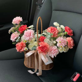 Basket of pink and coral carnations with white daisies on a car seat