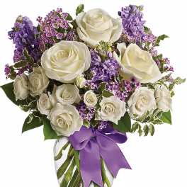 White roses and purple flowers in a glass vase with a purple ribbon