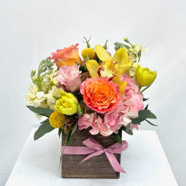 Colorful flower arrangement in a wooden box with a pink ribbon