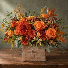 Orange roses and chrysanthemums in a wooden box with autumn leaves