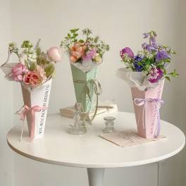 Three small pastel flower bouquets in tall gift boxes on a round table