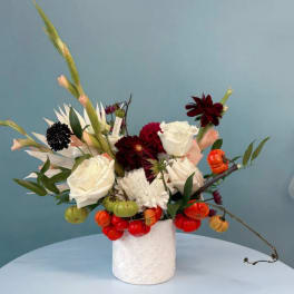 White and burgundy floral arrangement in a white vase with small pumpkins