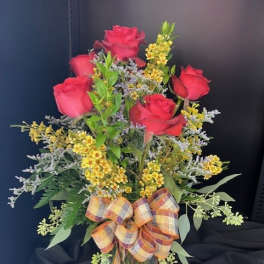 Red roses in a glass vase with yellow filler flowers and a plaid bow