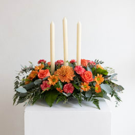 Orange and pink floral centerpiece with three ivory taper candles