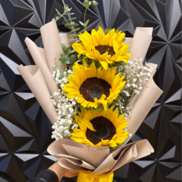 Wrapped bouquet of three yellow sunflowers with white filler flowers and a yellow ribbon.