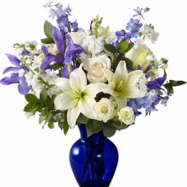 White lilies, roses, and purple flowers in a blue glass vase