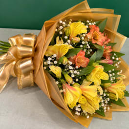 Bouquet of yellow and coral alstroemeria wrapped in gold paper with a ribbon