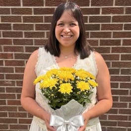 Woman holding a bouquet of yellow chrysanthemums wrapped in white paper with a bow
