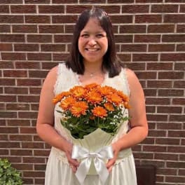 Woman holding a bouquet of orange daisies wrapped with a white ribbon