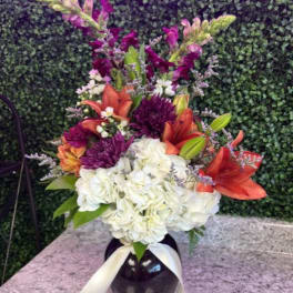 Bouquet of white hydrangeas, orange lilies, and purple blooms in a dark vase