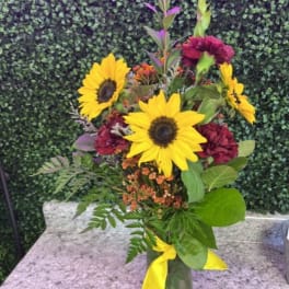 Sunflowers and burgundy flowers in a glass vase with a yellow ribbon