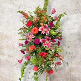Tall mixed floral arrangement with pink lilies, roses, and green accents on a stand