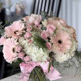 Pink gerbera daisies and roses in a glass vase with a pink ribbon