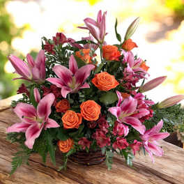 Pink lilies and orange roses arranged in a low basket centerpiece