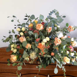 Low floral arrangement with peach roses and mixed greenery on a wooden surface