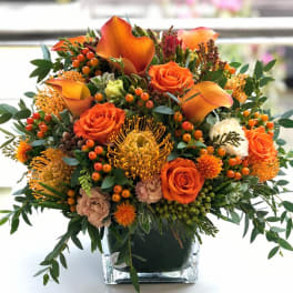 Orange and cream floral arrangement in a square glass vase