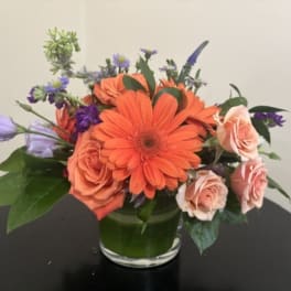 Orange gerbera daisies and peach roses in a glass vase