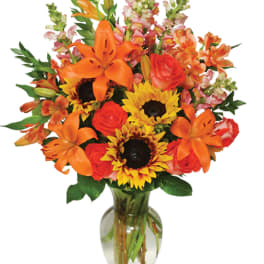 Orange lilies, roses, and sunflowers in a glass vase