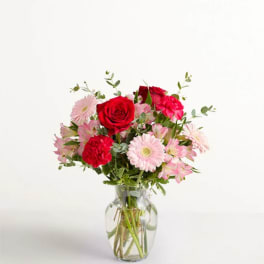 Pink and red mixed flowers arranged in a clear glass vase