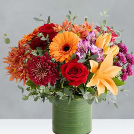 Mixed bouquet of orange, red, and purple flowers in a green vase