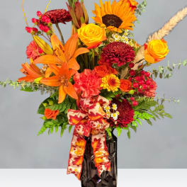 Orange and red mixed flower arrangement in a dark vase with a patterned ribbon