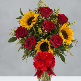 Red roses and sunflowers in a glass vase with a red bow