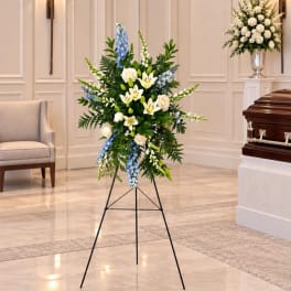 Standing funeral spray with white lilies, roses, and blue flowers on an easel