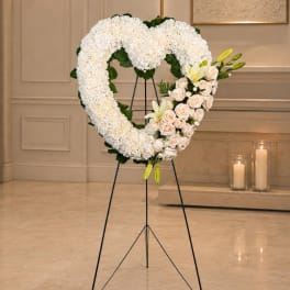 Heart-shaped white floral standing spray with pale roses and lilies