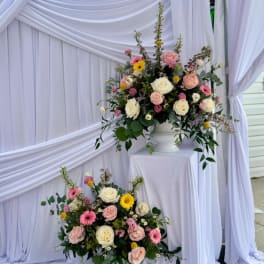 Two pastel floral arrangements on white pedestals with roses and daisies