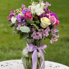 Mixed bouquet of roses and purple flowers in a glass vase with a lavender ribbon